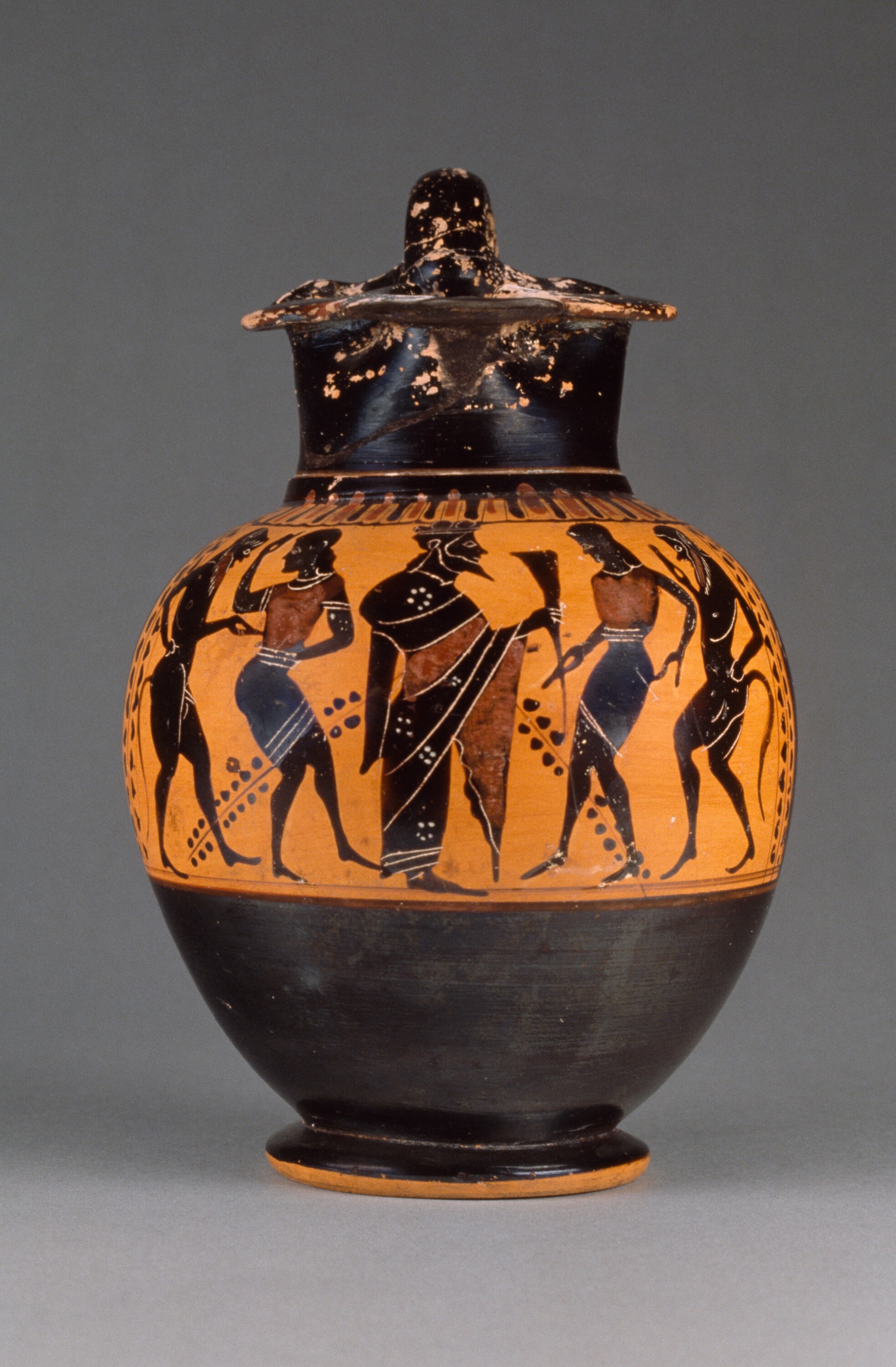 Œnochoé à figures noires, vers 510 avant J.-C. On peut voir au centre Dionysos représenté de profil avec une corne à boire. À ses côtés se tiennent des ménades (adoratrices de Dionysos) et des satyres en train de danser.